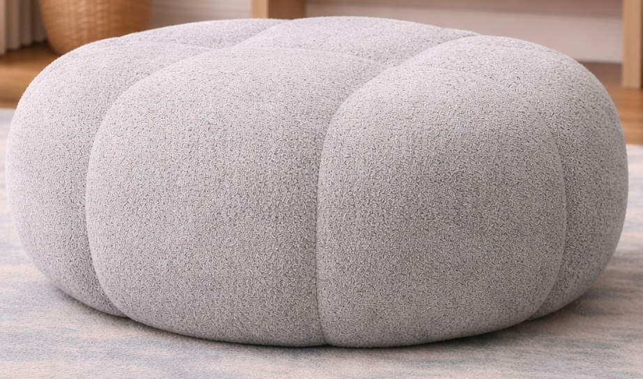 Gray ottoman in a living room setting with a rug, table, and chair.