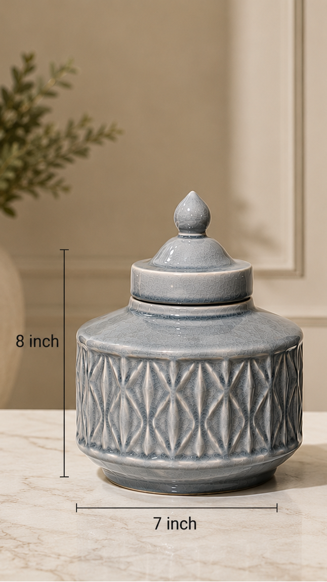 Two round lidded ceramic jars in a light blue-gray glaze with textured geometric patterns, shown on a marble surface with dimension lines indicating 7-inch width and 8-inch and 10-inch heights.