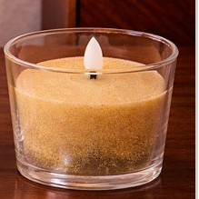 Two glass candle holders with sand-like texture and lit candles on a wooden surface.