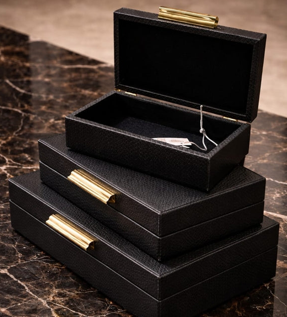 Set of black jewelry boxes with gold accents on a marble surface