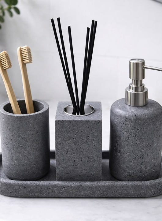 Bathroom set with gray concrete containers holding toothbrushes, diffuser sticks, and a soap dispenser on a marble surface.