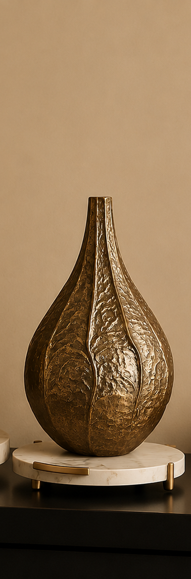 Two metallic teardrop-shaped decorative vases with a textured, leaf-like embossed pattern in a warm gold finish, displayed on round white marble bases on a dark console table.