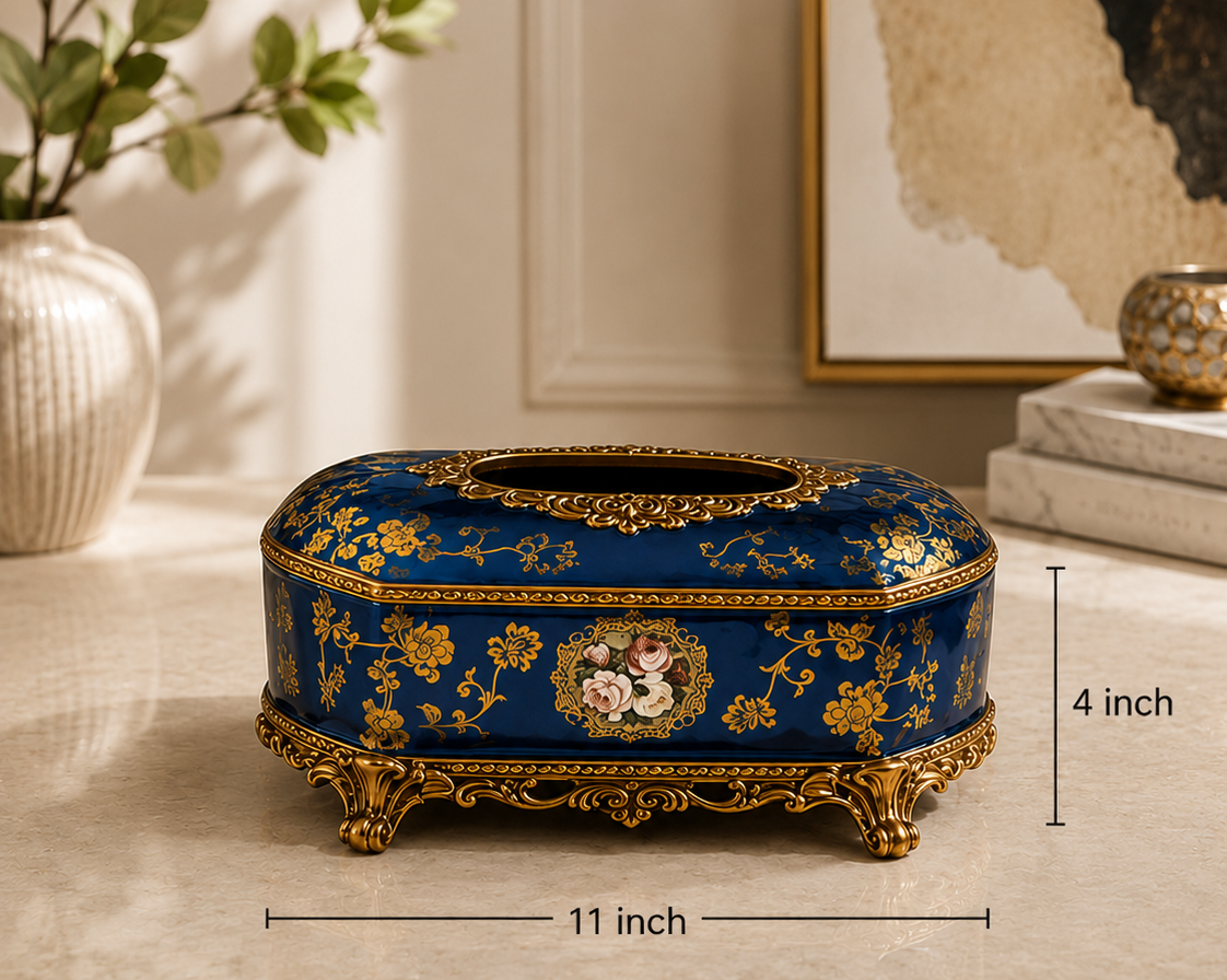 A decorative tissue box cover or small storage box with a royal blue and gold floral design, shown on a beige tabletop with dimension markers reading 11 inch by 4 inch. Text below lists material, finish, color, style, and dimensions.