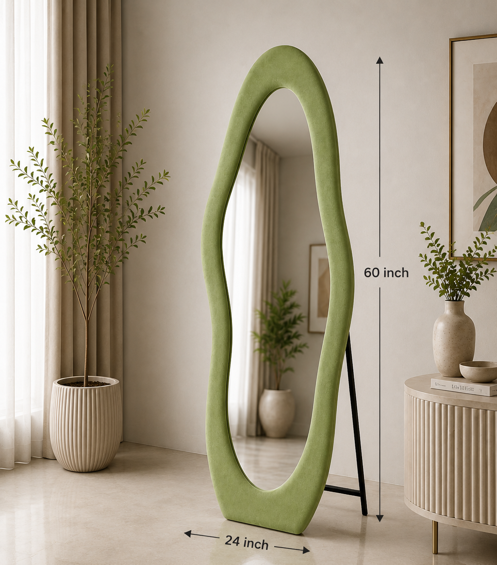 An asymmetrical floor mirror with a light sage green frame stands on a black easel in a styled room. The image includes dimension markers showing the mirror is 60 inches tall and 24 inches wide, with informational text at the bottom detailing stand type, stability, and dimensions.