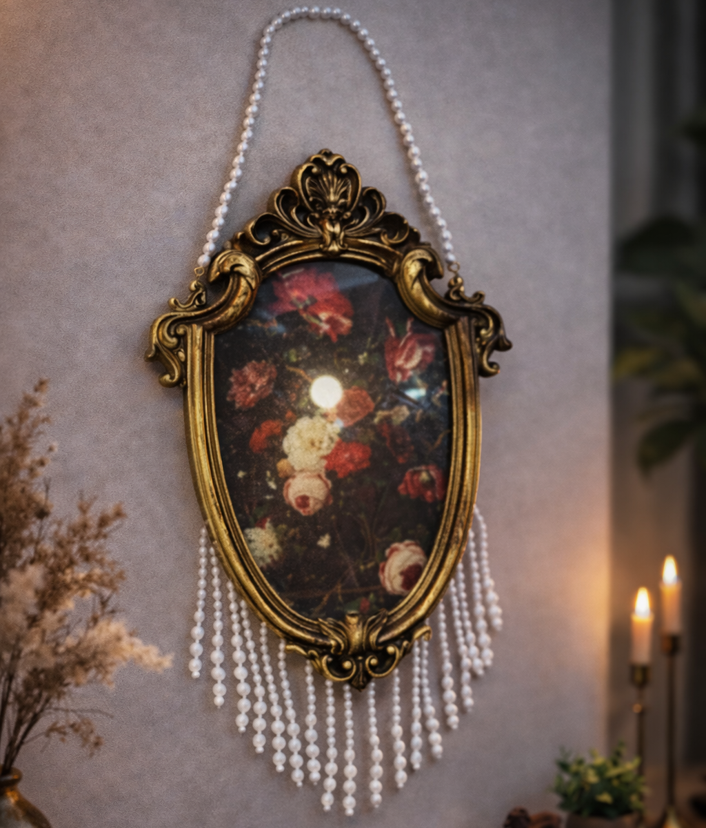 Decorative wall mirror with floral painting and pearl chain on a wall.