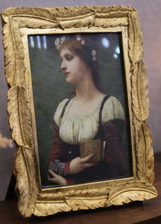 Vintage-style portrait in a gold frame on a wooden surface with a candlelit background.