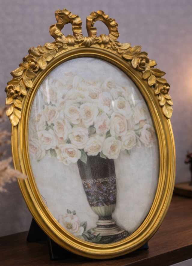 Decorative gold-framed picture on a shelf with a floral arrangement.