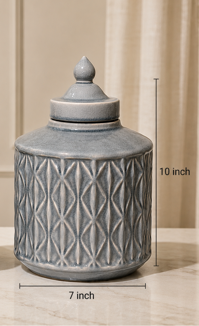 Two round lidded ceramic jars in a light blue-gray glaze with textured geometric patterns, shown on a marble surface with dimension lines indicating 7-inch width and 8-inch and 10-inch heights.