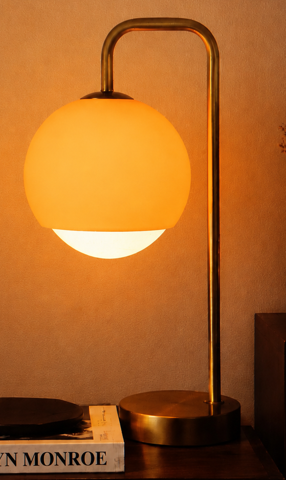 Table lamp with a warm glow on a surface next to a book titled 'Marilyn Monroe'.