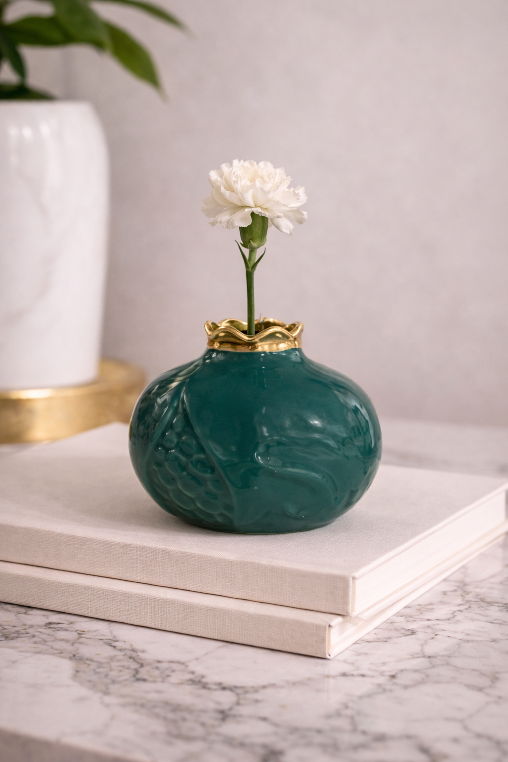 Green vase with a gold rim and white flower on a marble surface