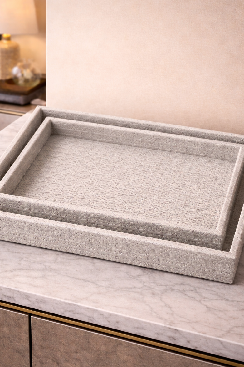 Two gray textured trays on a marble surface with a lamp in the background