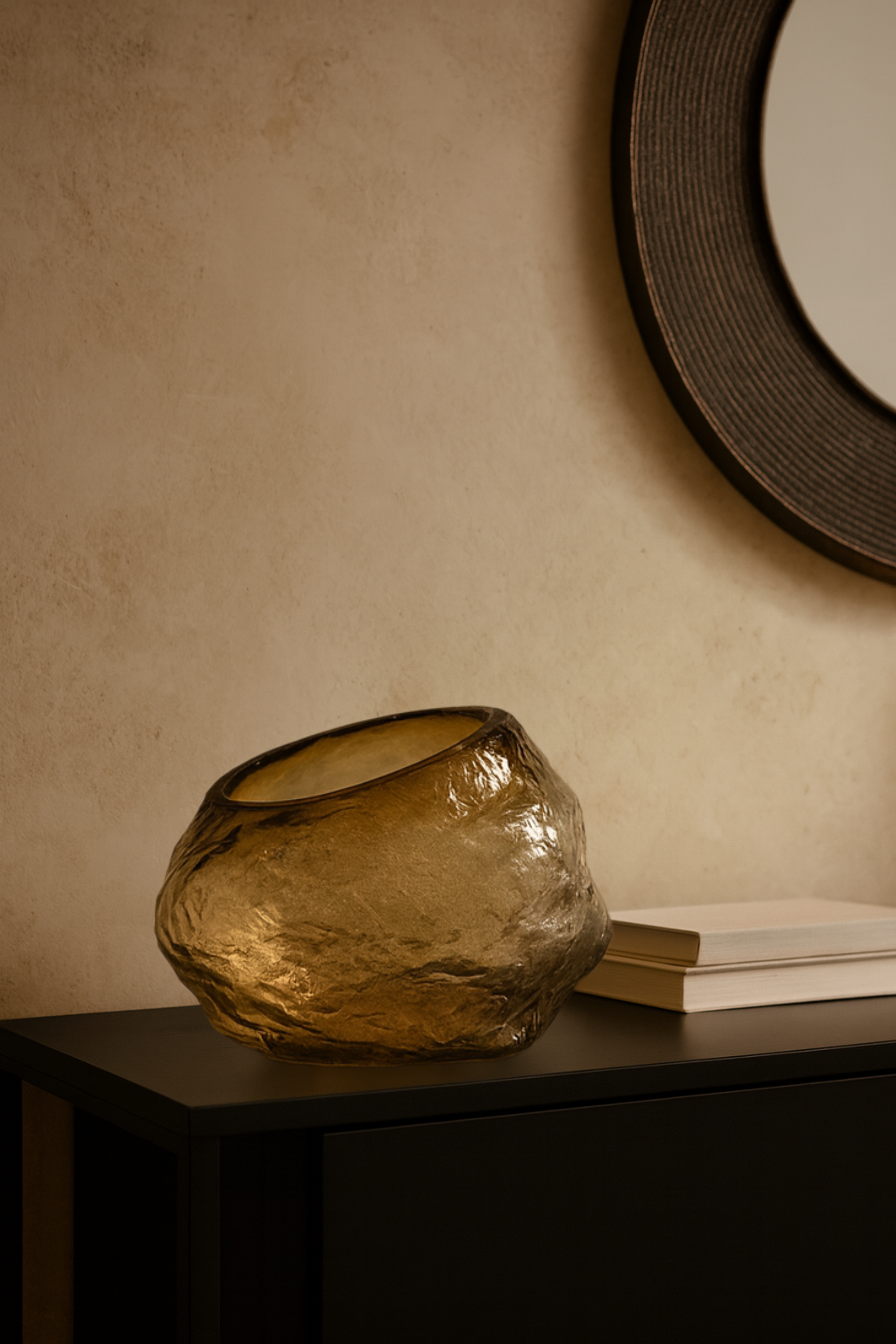 Glass vase on a dark surface with a beige wall and round mirror in the background