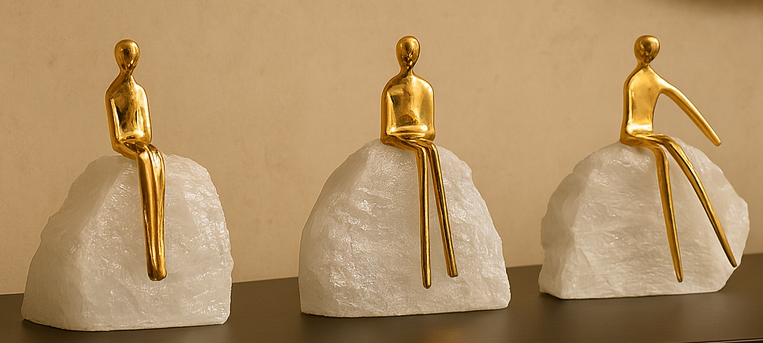 Three gold figurines sitting on white rock-like bases against a beige background