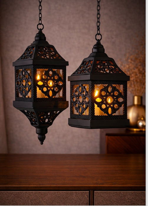 Two black metal hanging lanterns with intricate designs on a wooden surface.