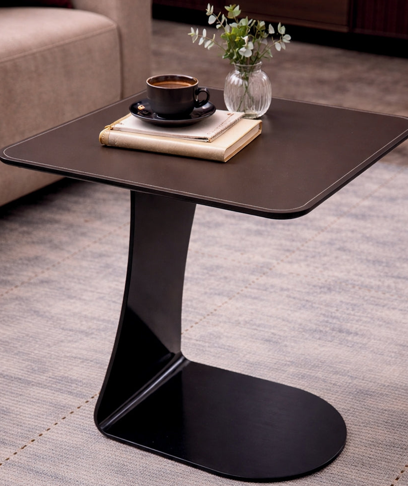 Modern black side table with a cup, saucer, and vase on a gray carpeted floor.