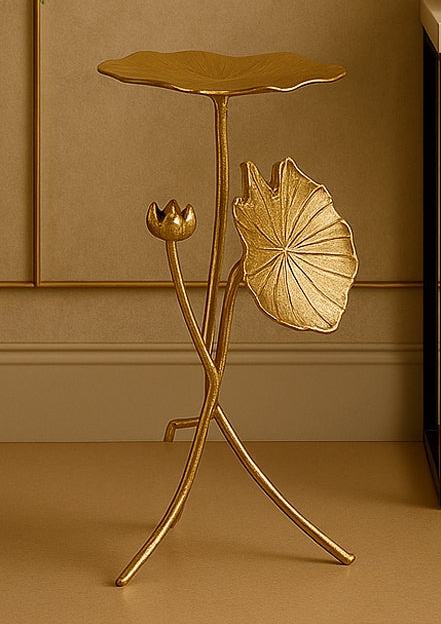 Gold side table with leaf design in a room with a plant and decorative items.