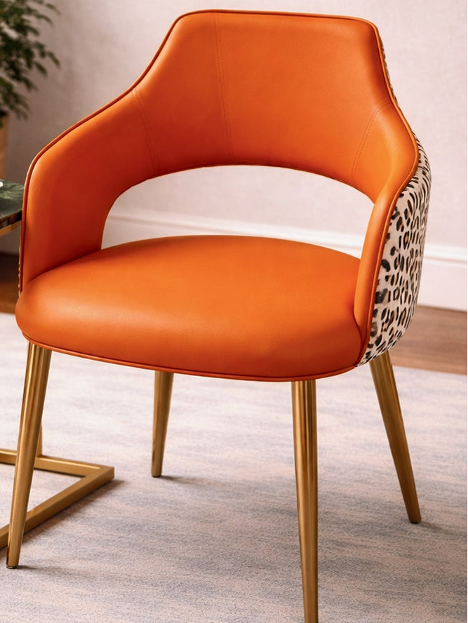 Orange chair with gold legs next to a small round table in a room setting.
