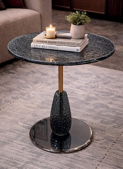 Small round table with a textured surface and metallic base on a carpeted floor.