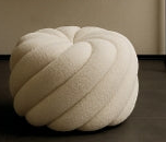 White textured pouf in front of a black console table with decorative items against a beige wall.