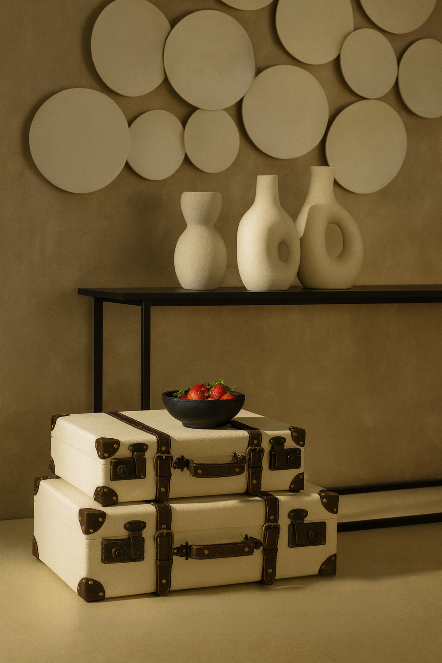 Stack of decorative boxes with a bowl of fruit on a table against a wall with circular decorations.