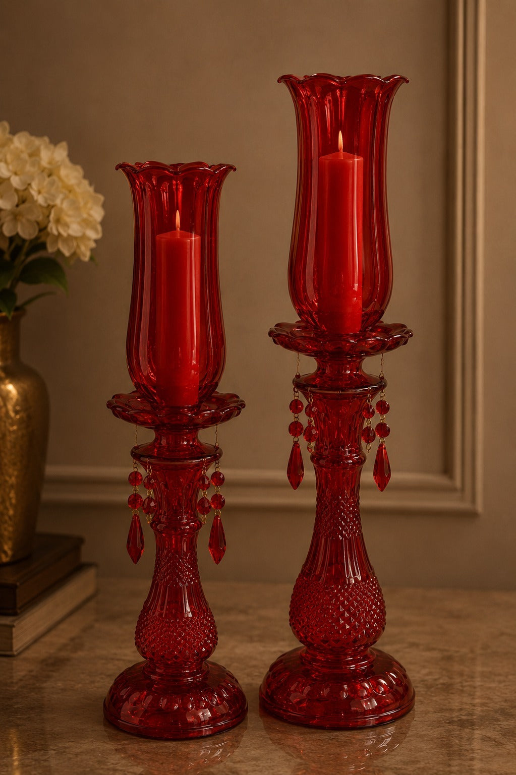 Two red glass candle holders with candles on a reflective surface.