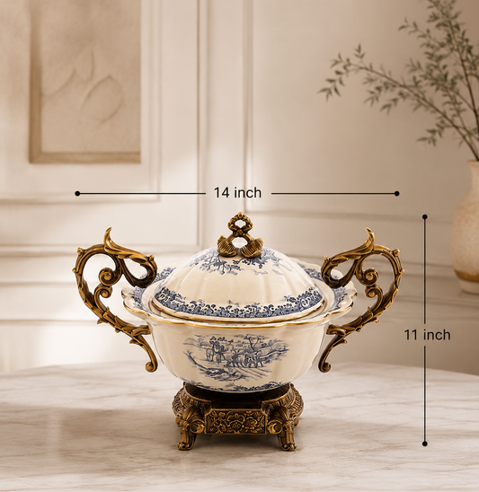 A decorative lidded serving bowl or tureen with ornate gold handles and base, blue floral porcelain pattern, and a cream-colored body, shown on a tabletop with overlaid dimension lines reading 14 inch across the top and 11 inch tall on the right. Small feature icons and text along the bottom mention premium ceramic and metal material, glossy finish, white/blue antique gold color, and dimensions.