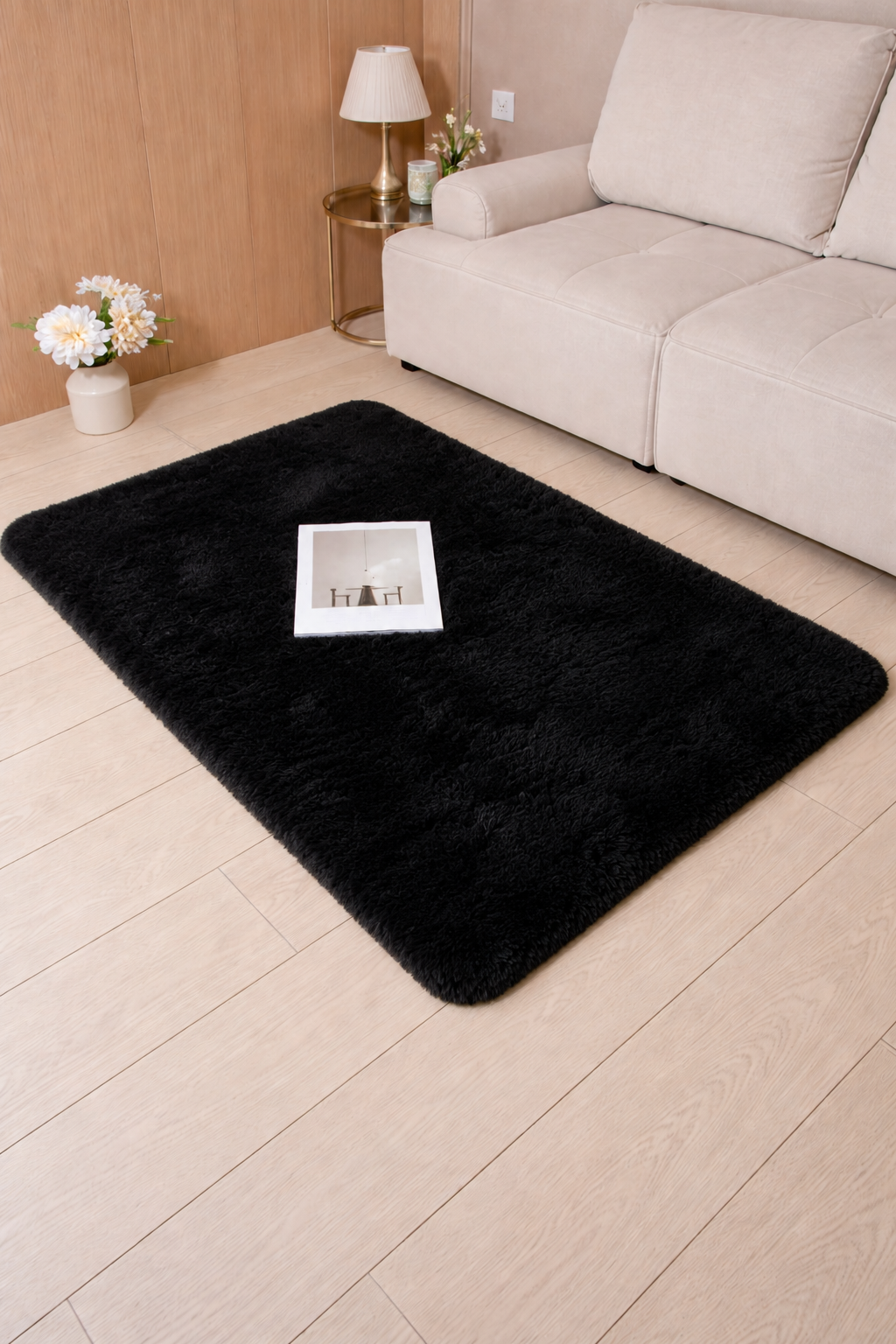 Black rug on a light wood floor in a living room setting with a beige sofa and side table.